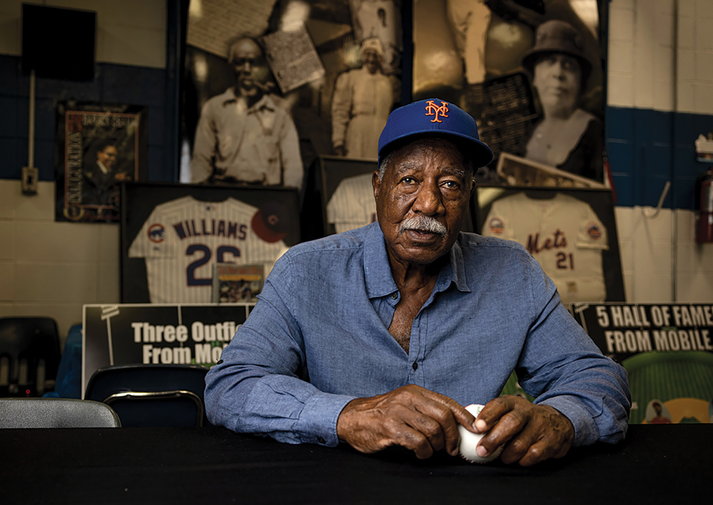 Cleon Jones holding a baseball in front of images and frames of mobile memorabilia